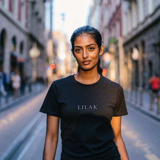 Black minimalist women’s t-shirt with lilac “LILAK” logo, worn by a confident woman on a European city street, premium casual streetwear style