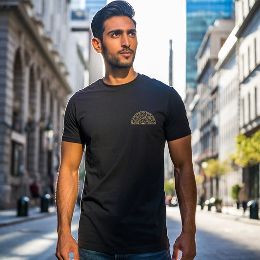 Male model wearing a black Supima cotton Lilak T-shirt featuring a gold mandala-inspired chest graphic, walking outdoors in an urban setting with modern glass buildings in the background