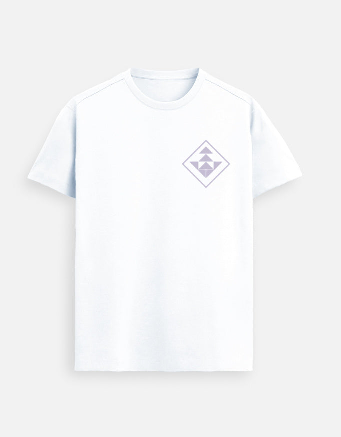 Woman standing in a stadium lounge wearing a White Lilak T-shirt with a purple geometric emblem on the left chest, with sunlight shining over the empty cricket ground in the background