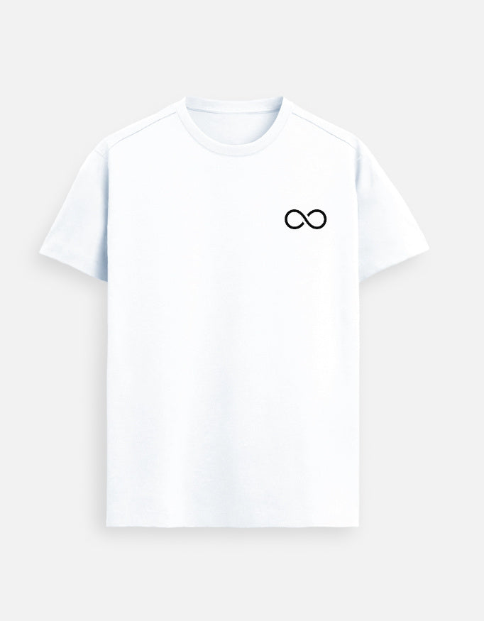 Man wearing a White Lilak T-shirt featuring a small black infinity symbol on the left chest, standing against a soft beige background with hands in pockets