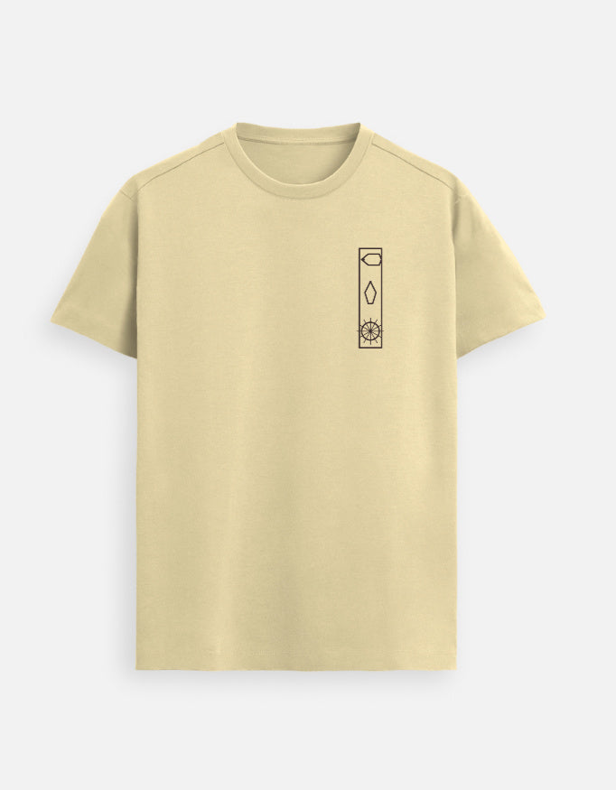 Woman walking down a sunlit city street wearing a light beige Lilak T-shirt with a minimal vertical graphic on the left chest, paired with blue 