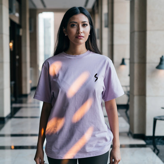Woman wearing a Lavender Lilak T-shirt featuring a small black minimalist ‘S’ symbol on the left chest, standing indoors in soft natural light with a calm expression