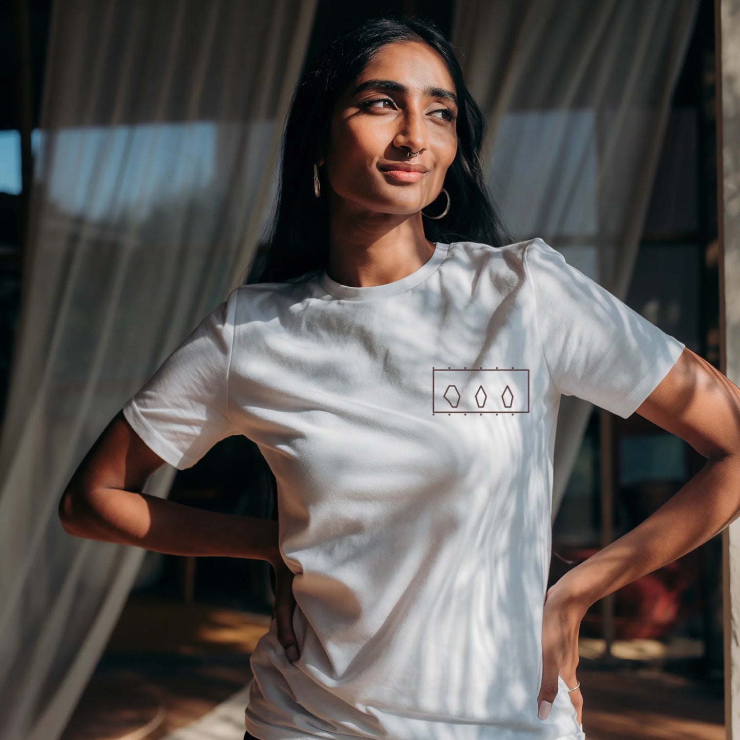 Woman standing inside a modern art museum wearing a White Supima cotton T-shirt by Lilak, featuring a minimal geometric design on the left chest