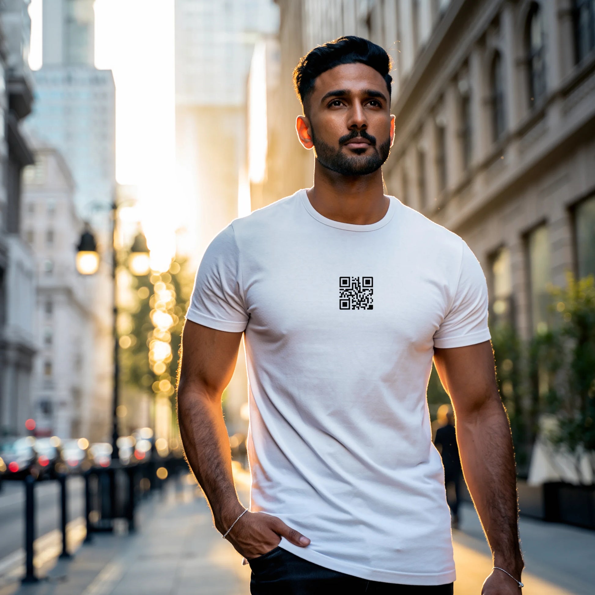 Man wearing a White T-shirt with a black QR code printed at the center of the chest, standing indoors in soft natural light with hands in pockets