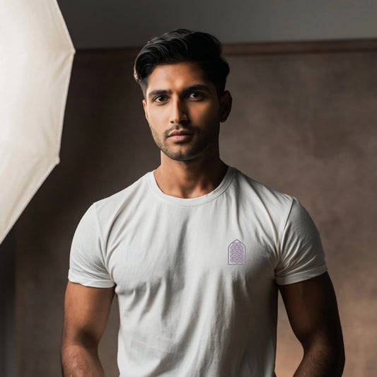 Indian male model wearing a White T-shirt with a purple geometric arch design on the chest, standing in a sunlit minimalist studio with soft shadows and a large window
